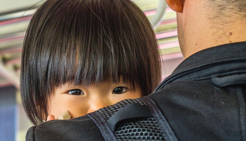Chinese child being held, peaking over shoulder of dad