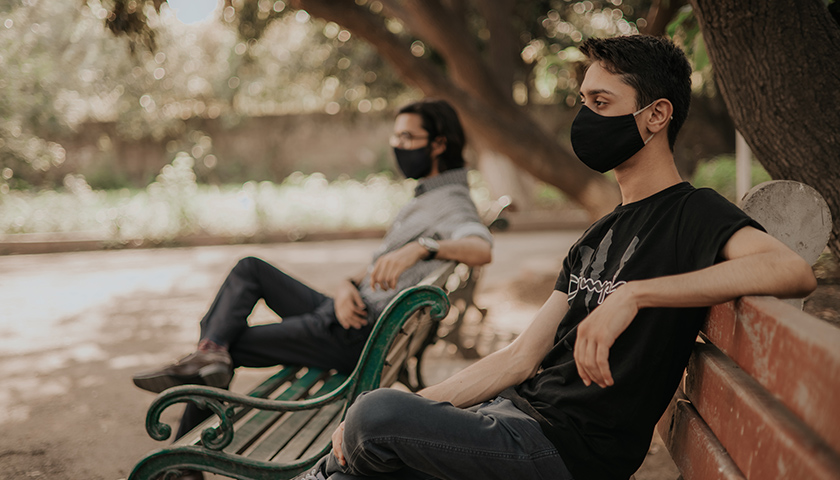 Two people wearing masks, on different benches, social distancing